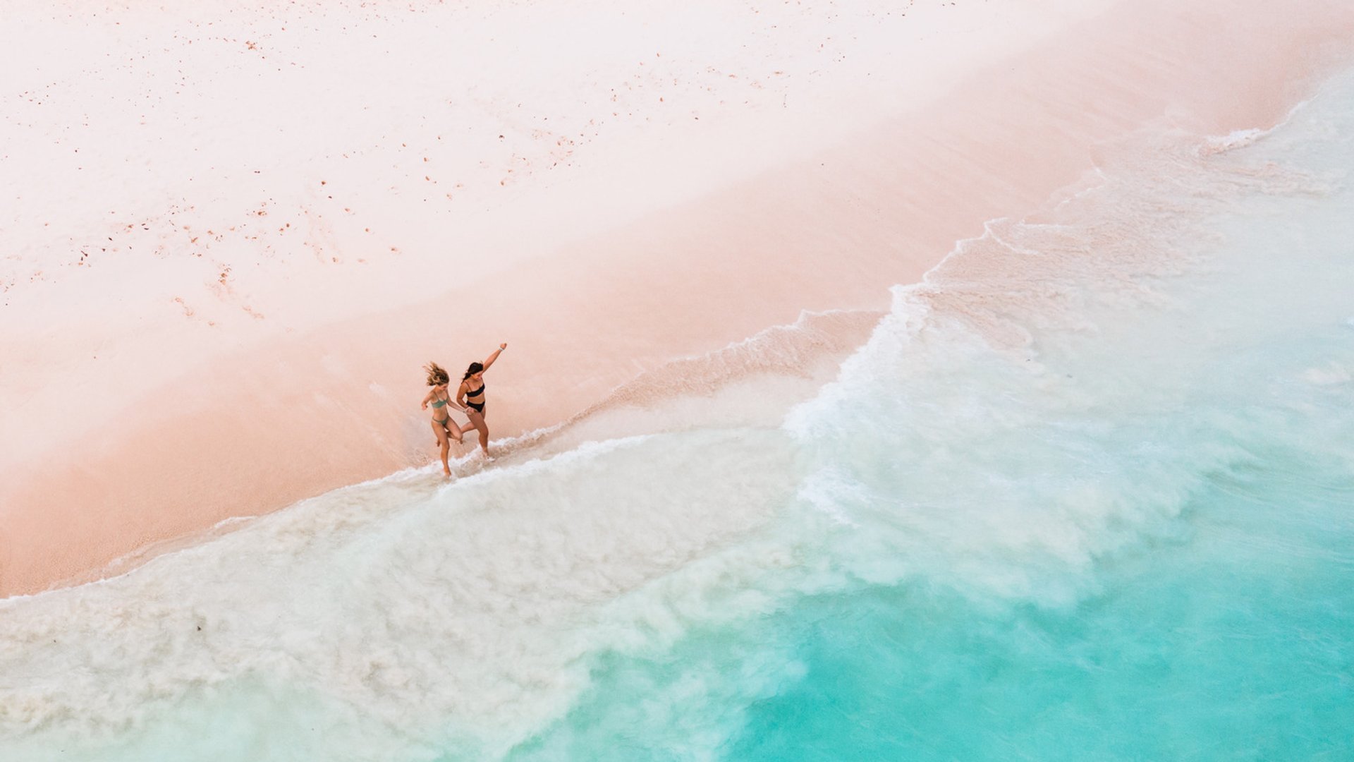 Two people walking on a pristine beach with turquoise waves gently lapping the shore.