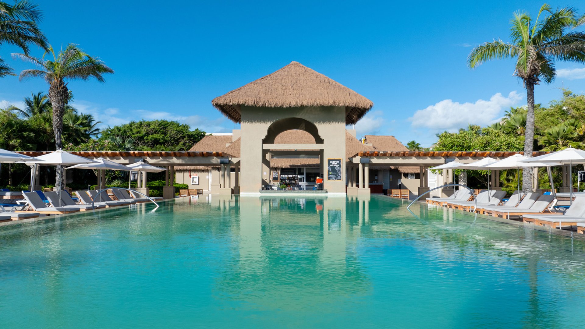 Eden Pool at Hard Rock Punta Cana, with lounge chairs, umbrellas, and tropical palm trees under a clear blue sky.