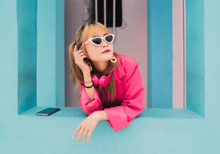 a woman wearing pink sunglasses and a pink shirt leaning on a blue wall